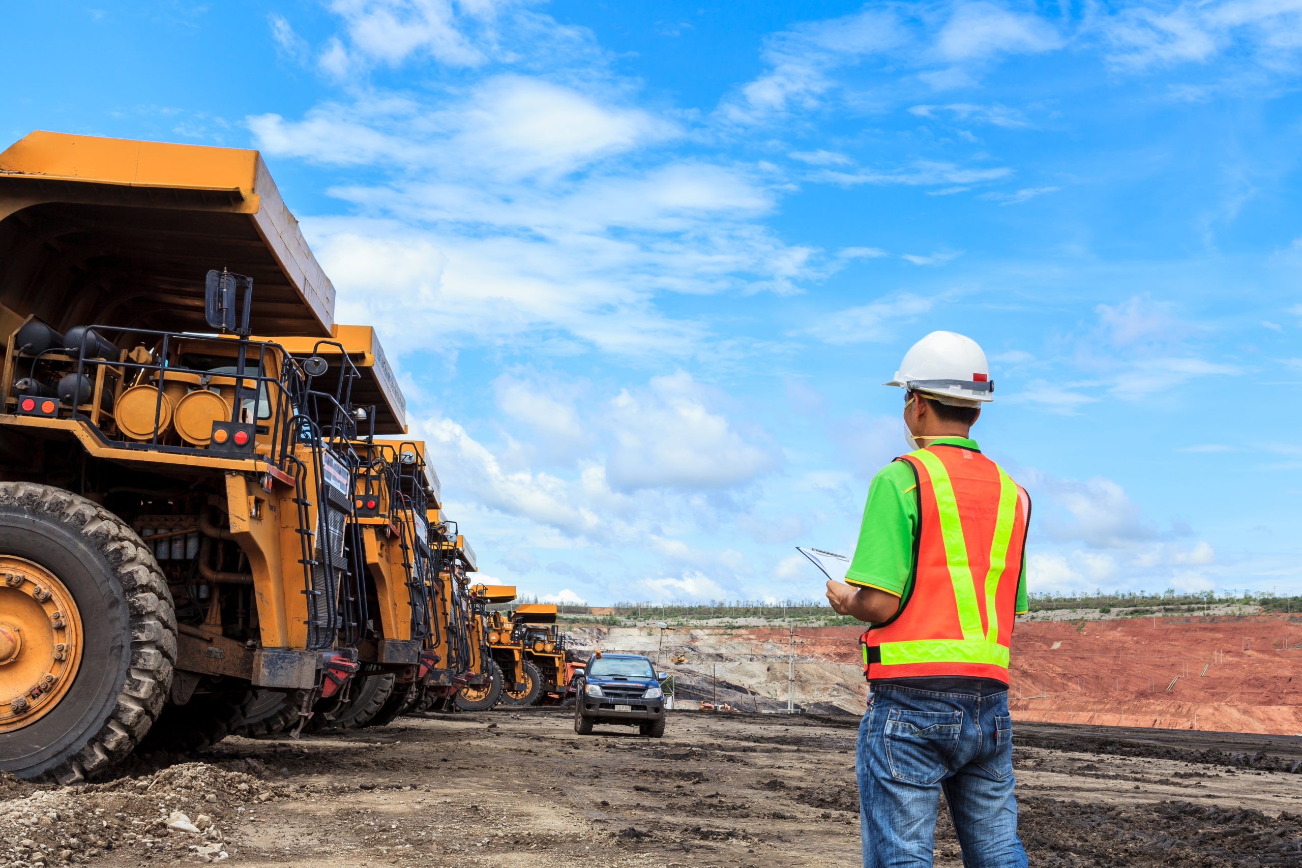 Worker wearing safety gear in an open lignite mine with heavy machinery in the background